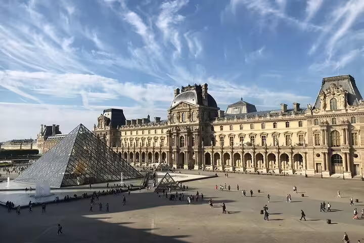 Louvre Museum glass pyramid and ornate palace facade with visitors in Paris courtyard