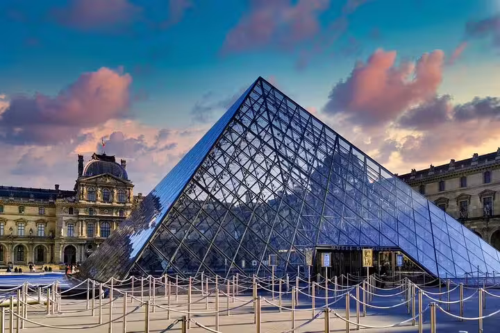 Glass pyramid entrance of the Louvre Museum in Paris at sunset with historic palace wings in background