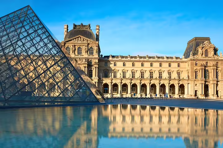 Louvre Museum with iconic glass pyramid under blue sky, reflecting in water, featured in Paris private tour with skip-the-line access.