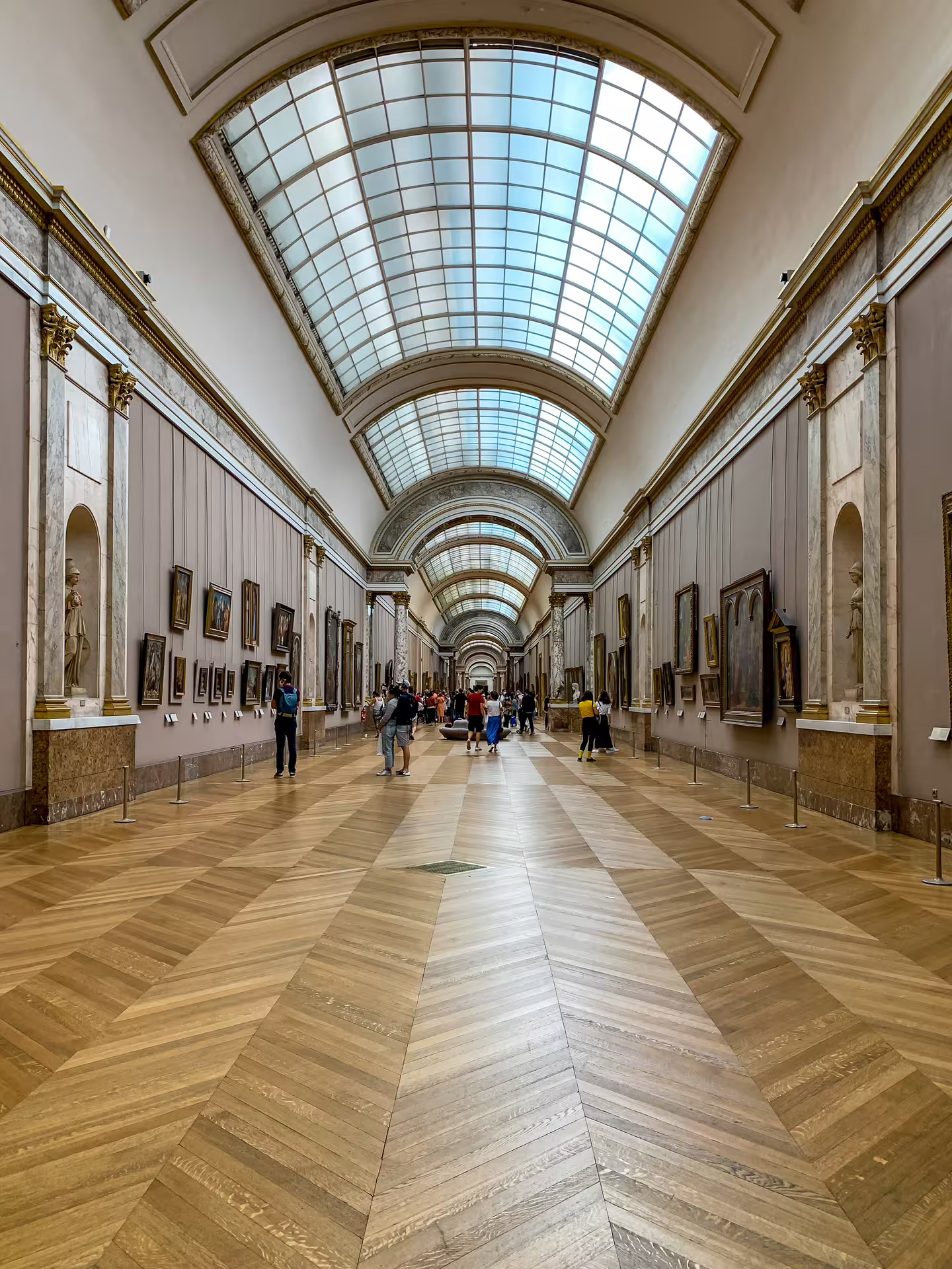 Grand Gallery of the Louvre Museum with skylight ceiling, parquet floors, and paintings on walls