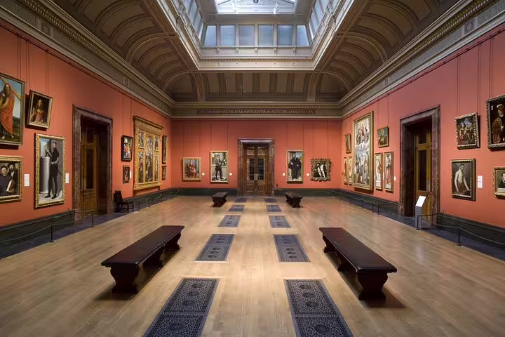 Grand museum gallery hall with Renaissance paintings on red walls and wooden benches at the Louvre