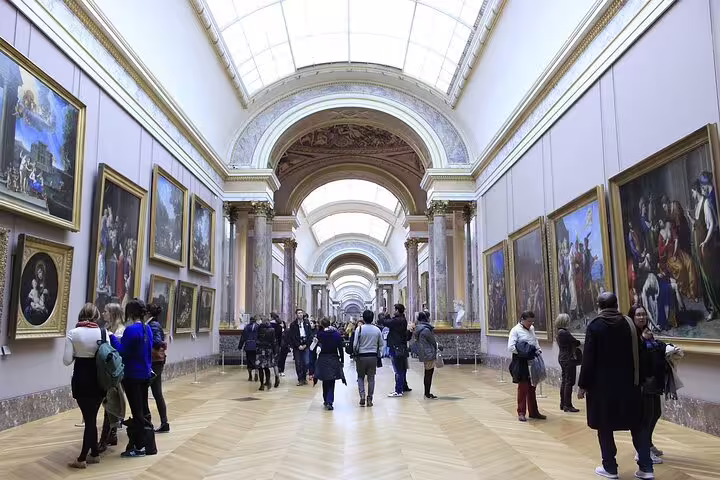 Visitors exploring a grand gallery hall at the Louvre Museum in Paris with large classical paintings on walls