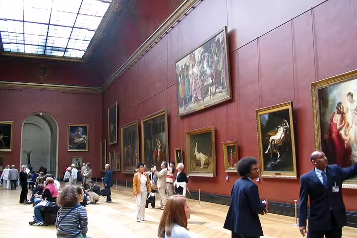 Visitors admiring large classical paintings in a grand red-walled gallery at the Louvre Museum, Paris