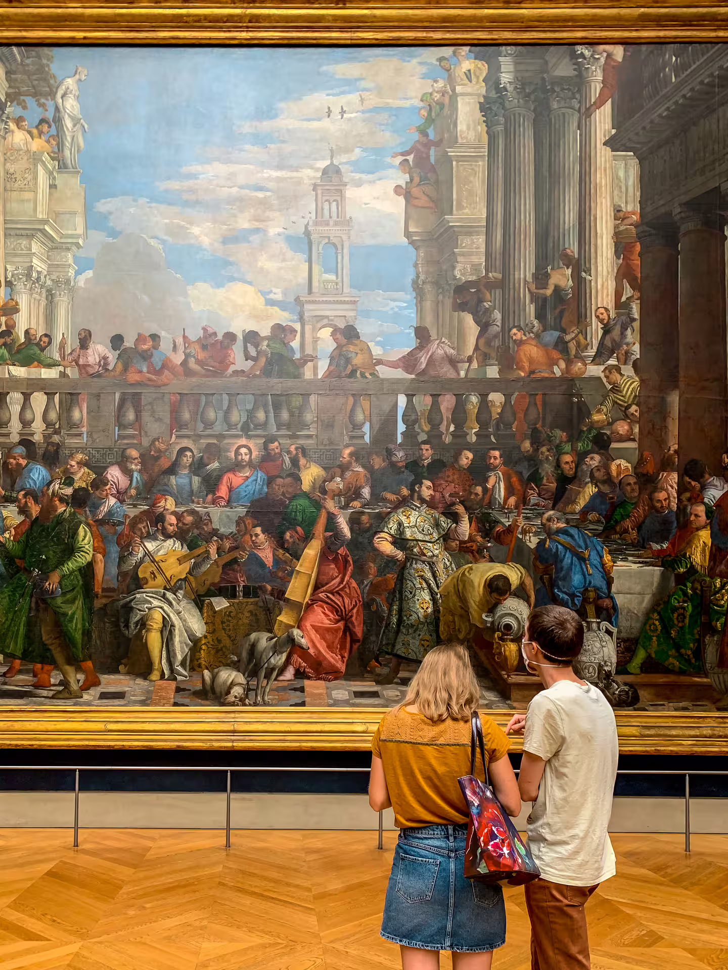 Two visitors admiring the Wedding at Cana painting by Veronese at the Louvre Museum in Paris