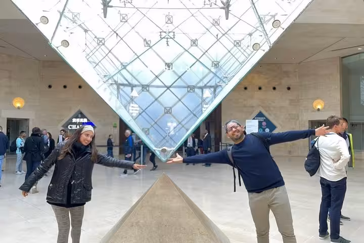 Visitors pose under the Louvre Pyramid inside the museum lobby on a guided group, private or solo tour in Paris