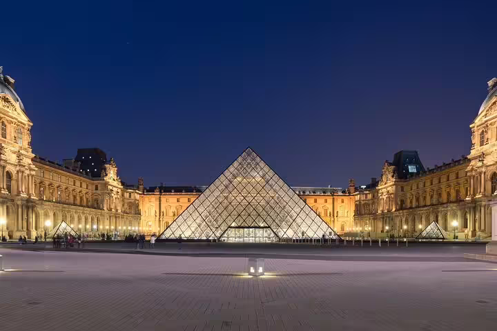Louvre Museum glass pyramid illuminated at night with classical palace wings in Paris