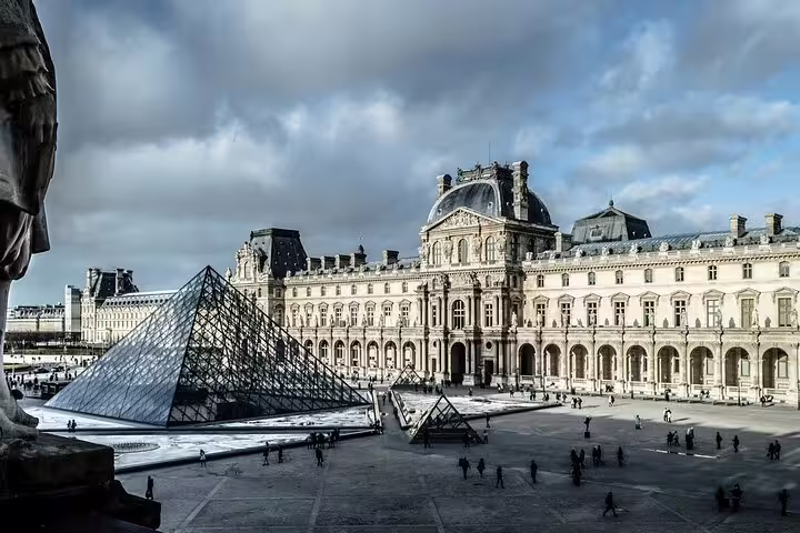 Louvre Museum glass pyramid courtyard with tourists on Paris panoramic city tour