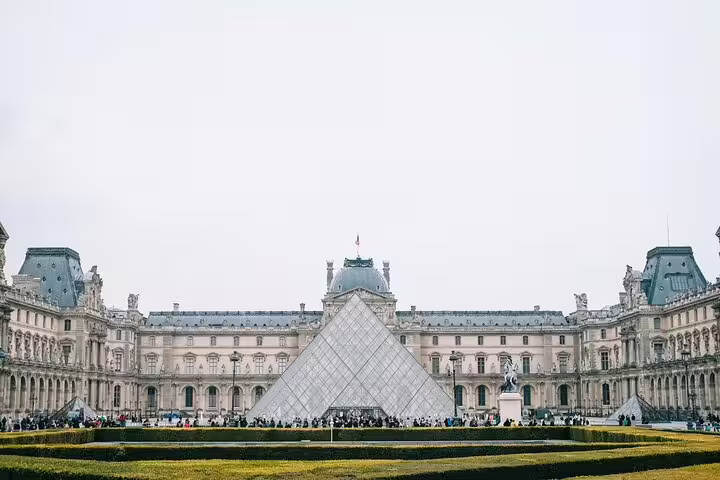Louvre Museum glass pyramid courtyard with tourists in Paris on an overcast day