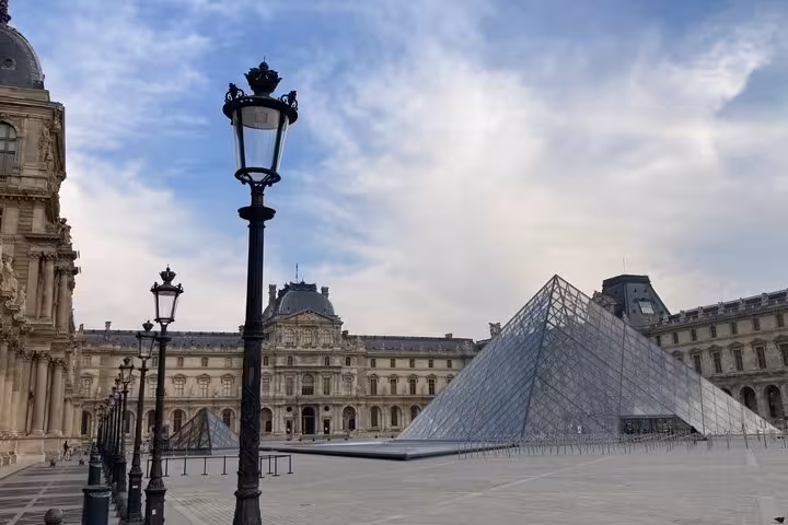 Louvre Museum glass pyramid and classical palace facade in Paris courtyard with lamp posts