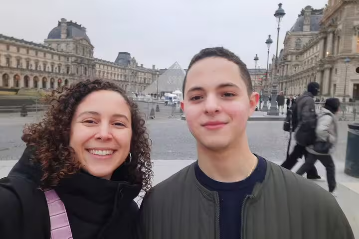 Two visitors smiling in front of the Louvre pyramid in Paris, France