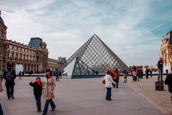 Tourists posing in front of the iconic glass Louvre Pyramid in Paris, France