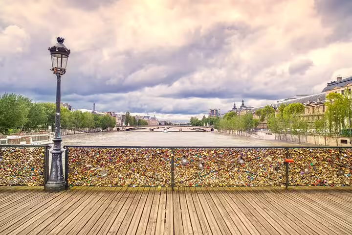 Love locks covering the railing of Pont des Arts bridge over the Seine River in Paris with cloudy sky