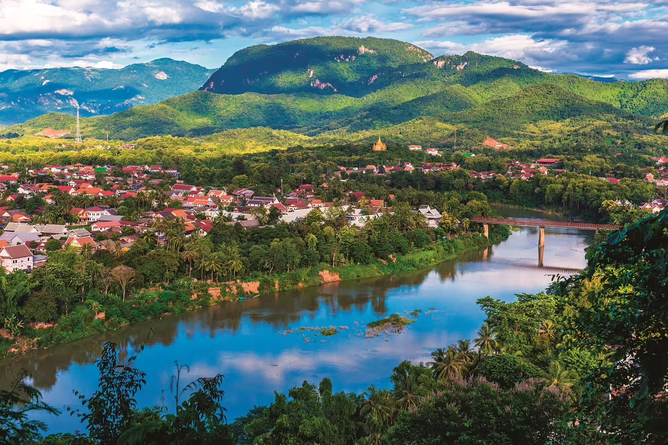 Scenic view of Luang Prabang with lush mountains and river, highlighting Laos' natural charm and vibrant culture.