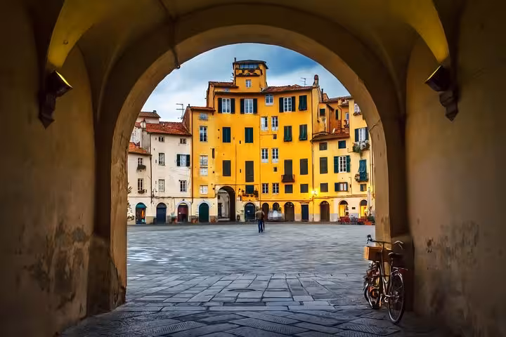 Charming Lucca square framed by archway, featuring vibrant yellow buildings, ideal for Pisa and Lucca day trips.