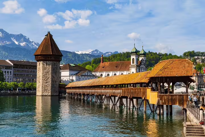 Scenic view of Chapel Bridge and Water Tower in Lucerne, surrounded by historic architecture and snow-capped mountains.