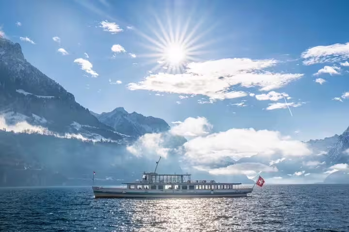 Scenic cruise on Lake Lucerne under a bright sun, surrounded by majestic Swiss Alps and clear blue skies.