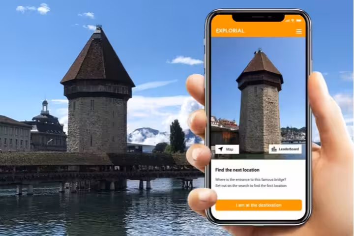 Phone app guiding Lucerne scavenger hunt tour at Chapel Bridge Water Tower with lake and Alps view