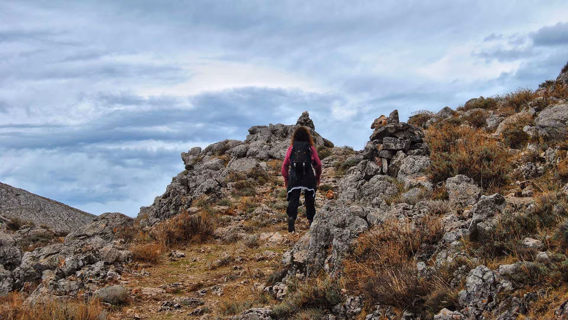 Hiker ascending rocky terrain under cloudy skies at Lula Montalbo, showcasing rugged outdoor exploration.