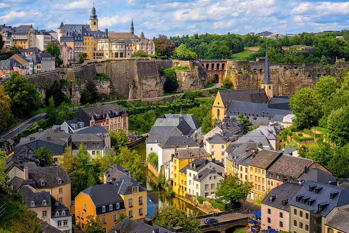 Panoramic view of Luxembourg City's Grund district with colorful buildings, medieval fortifications, and lush greenery