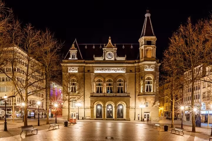 Luxembourg City municipal building illuminated at night with cobblestone plaza and bare winter trees
