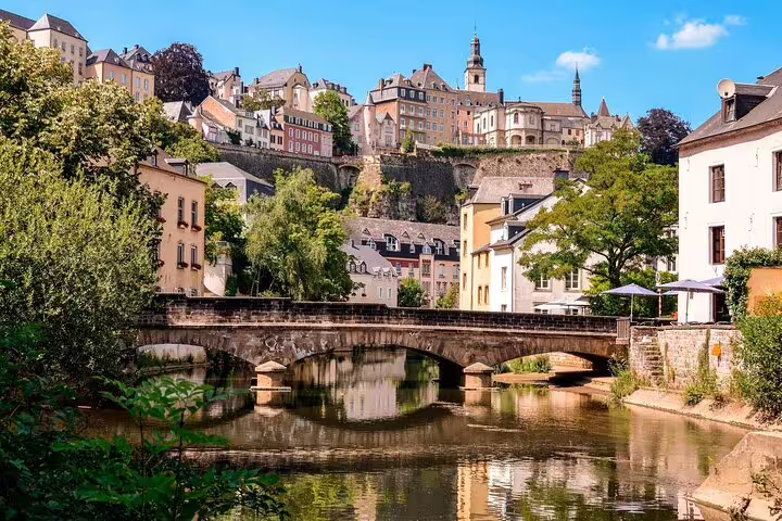 Stone arch bridge over the Alzette River with historic Luxembourg City buildings and cliffs in background