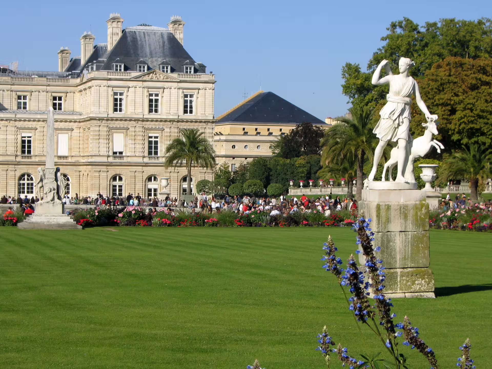 Luxembourg Palace and gardens with white Diana statue, manicured lawns, colorful flowerbeds and visitors in Paris