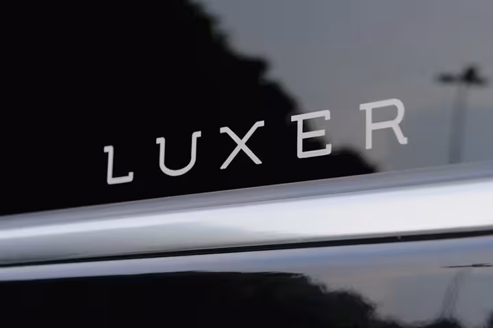 Close-up of Luxer logo on a sleek black vehicle, offering premium transfer from Venice to Cortina d'Ampezzo.