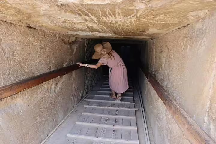 Visitor descending narrow passage in an ancient Egyptian tomb, included on 8-day Luxor Nile cruise and Cairo tour