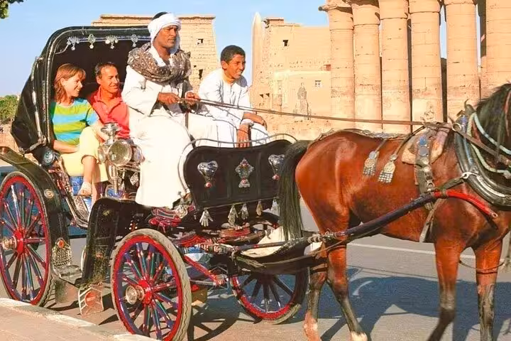 Tourists riding a horse carriage past Luxor Temple columns on a Nile Corniche city tour in daylight