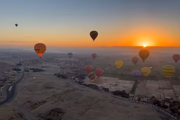 Multiple hot air balloons drifting over Luxor at sunrise, panoramic Egypt flight above ancient monuments
