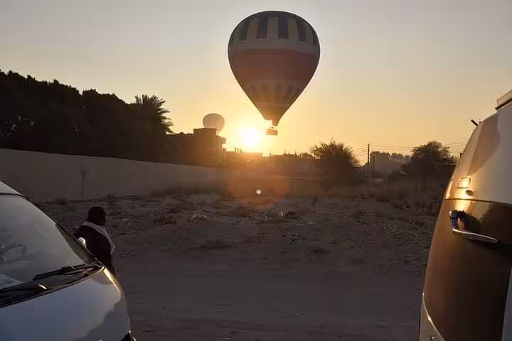 Luxor sunrise hot air balloon drifting above rooftops, VIP ride pickup scene before takeoff in Egypt