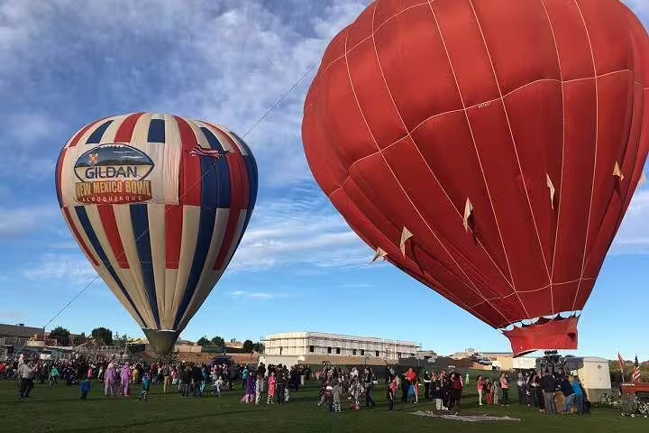 Colorful hot air balloons inflating on a field with crowds, pre-flight scene for a Luxor sunrise balloon ride