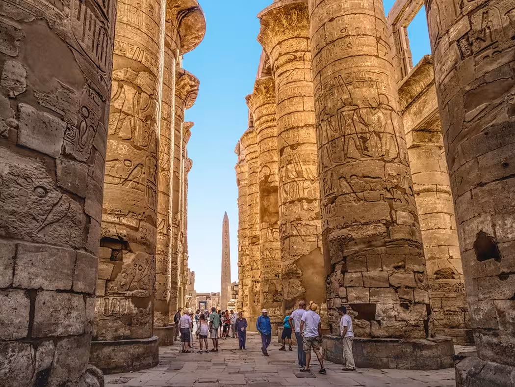 Tourists walk between towering Karnak Temple columns in Luxor on a full-day guided tour of ancient Egypt