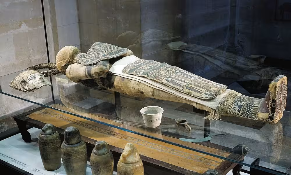 Mummification Museum Luxor exhibit with wrapped mummy and canopic jars in glass case on guided Luxor tour