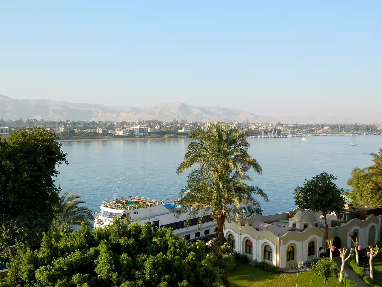 Nile River view in Luxor with cruise boat and palm trees, scenic stop on Hurghada to Luxor minibus tour