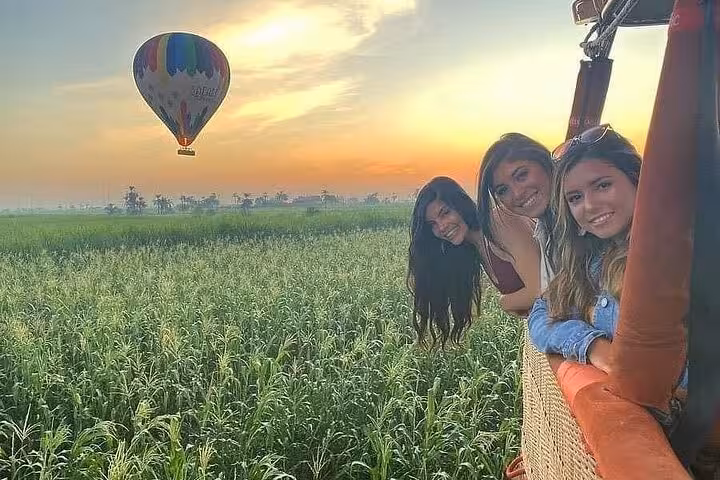 Friends leaning from balloon basket over Luxor fields at sunrise, Nile River Valley hot air balloon tour view