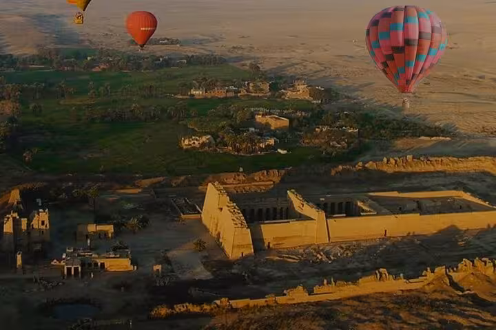 VIP Luxor sunrise hot air balloon tour with hotel transfer, soaring over Habu Temple and green Nile fields
