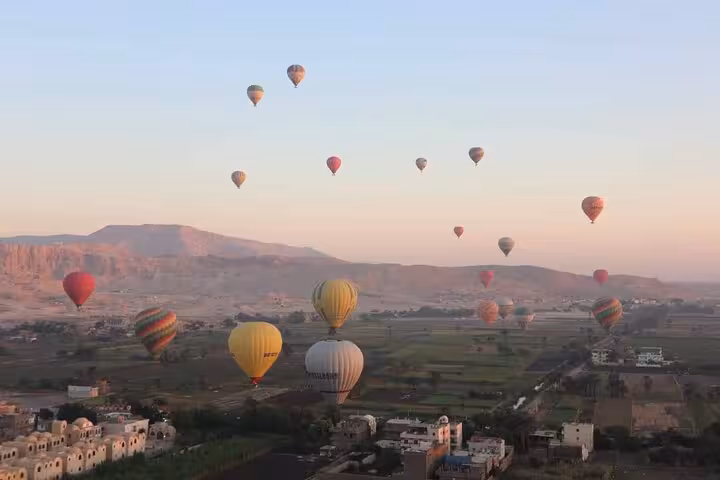 Luxor sunrise hot air balloon tour floating over the Nile Valley and villages, with distant desert hills