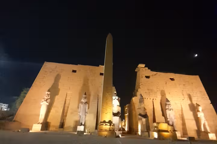 Luxor Temple illuminated at night with a prominent obelisk and statues, creating a stunning historical scene.