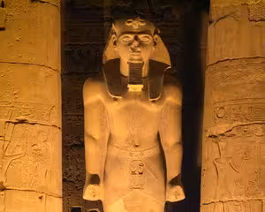 Illuminated ancient Egyptian pharaoh statue at Luxor Temple colonnade at night