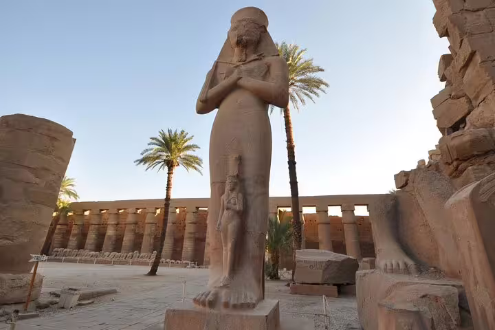Ancient pharaonic statue in Luxor Temple courtyard with palm trees on Luxor day trip by plane from Sharm El Sheikh
