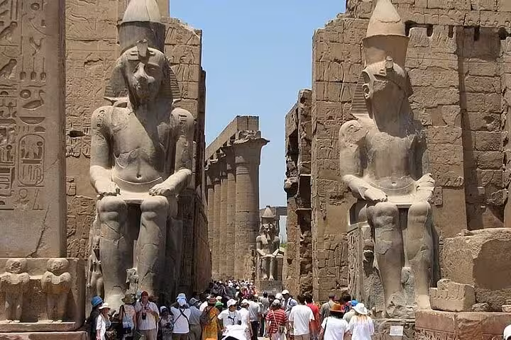 Tourists explore the grand entrance of Luxor Temple, flanked by imposing ancient statues on the West Bank of the Nile.