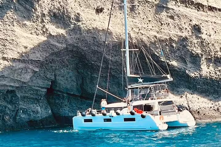 Luxurious catamaran anchored near Santorini's dramatic cliffs on a tailor-made private cruise experience.