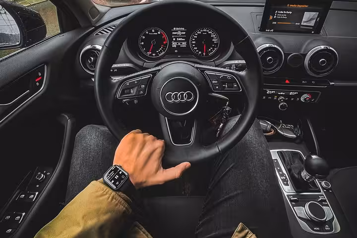 Premium Audi interior with professional driver’s hand on wheel, representing luxury private Muscat airport transfer experience