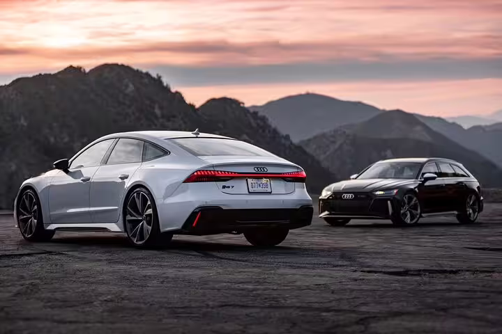 Two Audi luxury sedans parked at sunset with mountain backdrop for private airport transfer
