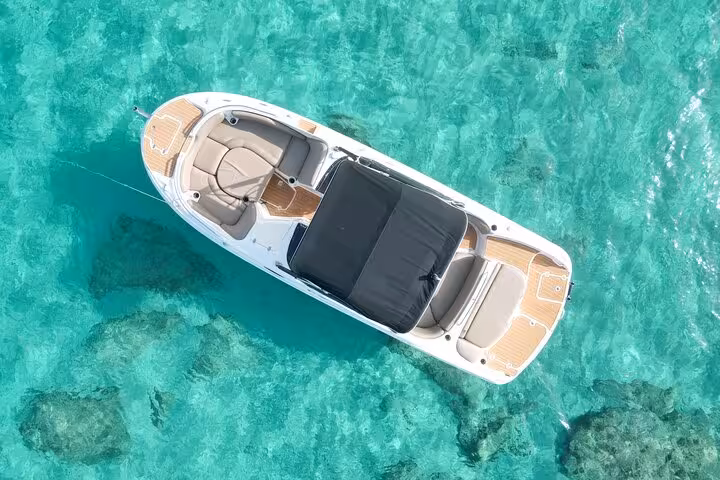 Aerial view of a luxury boat floating in crystal-clear waters near Cala Comte on a sunny day.