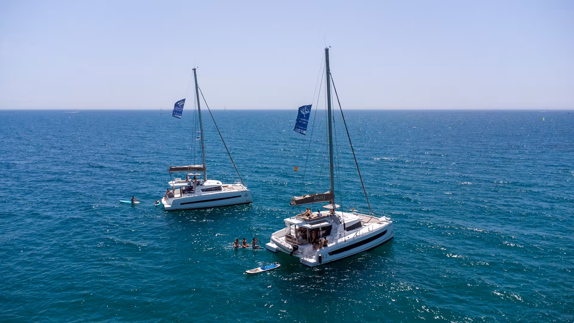Aerial view of Bali 4.2 luxury catamarans off Barcelona with guests swimming and paddleboarding on a private cruise