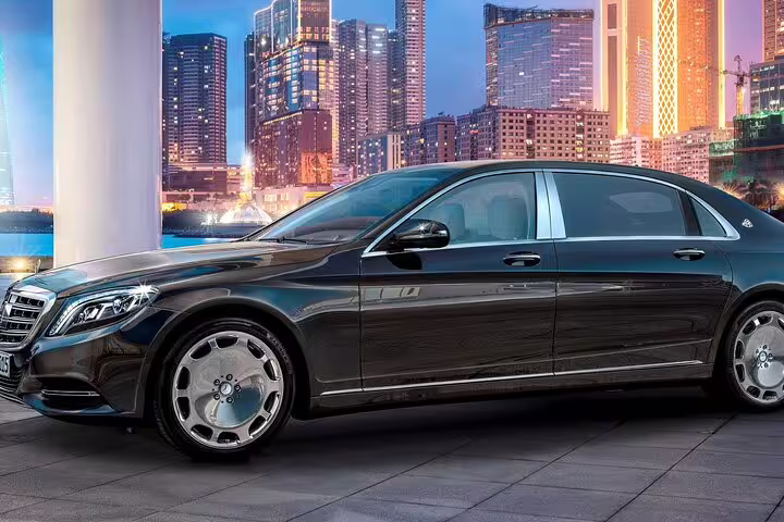 Black Mercedes-Maybach luxury sedan parked in front of illuminated city skyline at dusk