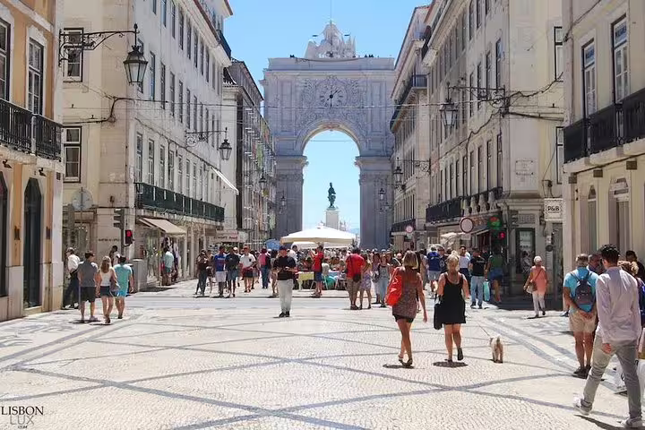 People strolling through Lisbon's vibrant shopping district near the iconic Rua Augusta Arch on a sunny day, ideal for outlet shopping.