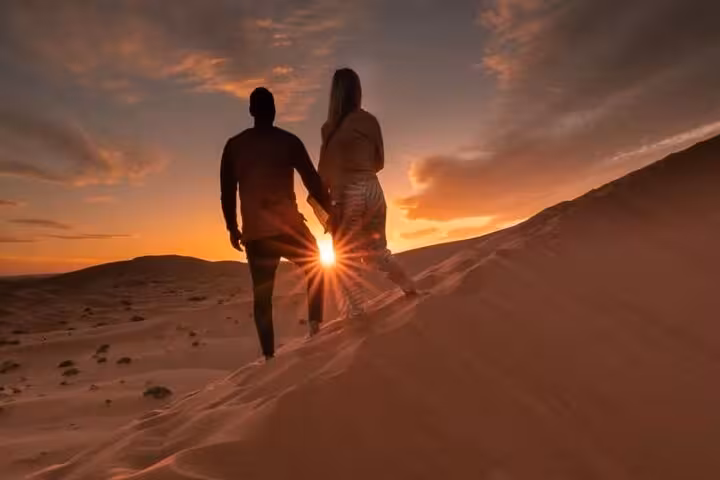 Couple holding hands, enjoying a romantic sunset on a sand dune during a luxury desert tour from Fes.
